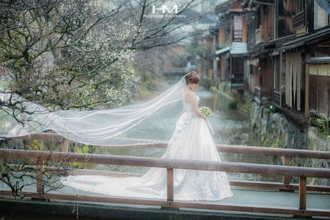 這張照片是一位美麗的新娘，她穿著潔白的婚紗，站在一座木橋上，橋下是潺潺流水，背景是一片綠意盎然的風景，畫面充滿了浪漫與幸福的氛圍。