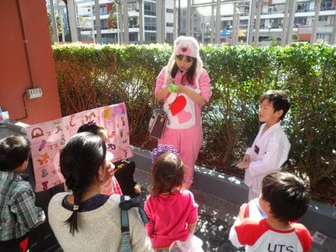 這張「兒童活動」的照片是一群小朋友在一個戶外場地參加活動，其中一個穿著粉紅色衣服的小女孩正在教小朋友學習字母。