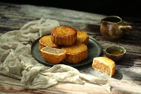 這張「月餅」的照片是幾塊月餅放在木頭桌子上，旁邊有一壺茶和一個茶杯。