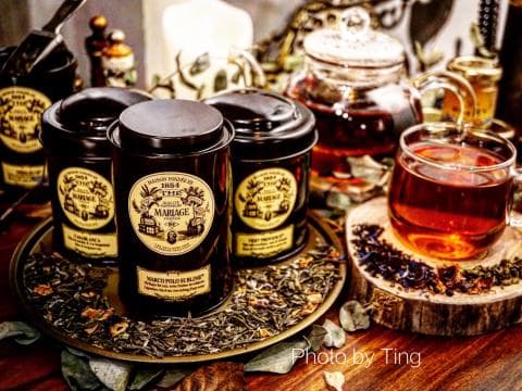 這張照片是四罐不同口味的茶葉罐，其中一罐的罐身上印著 1894 THE TEA MARRIAGE 字樣，旁邊放著一杯茶和一片放滿茶葉的木頭。