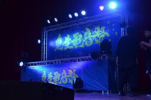 這張「舞臺表演」的照片是舞臺上佈置了黃色的招牌，兩個表演者正在舞臺上表演，舞臺上也有燈光照明。