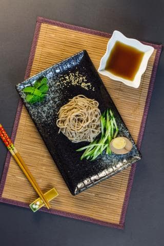 這張「涼麵」的照片是涼麵放在黑色盤子上，搭配黃瓜絲、醬油和半顆蛋。
