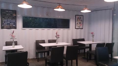 這張餐廳的照片是一個簡約的空間，有白色的牆壁、木地板和幾張桌子和椅子。牆上有一個黑色的告示牌，桌上放著花和玻璃瓶。牆上還有一個窗戶，可以看到外面的景色。