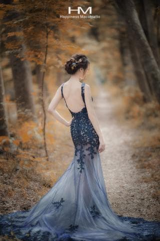 這張照片是一個穿著藍色蕾絲婚紗的女子，她在一片秋天的森林中，顯得優雅而美麗。