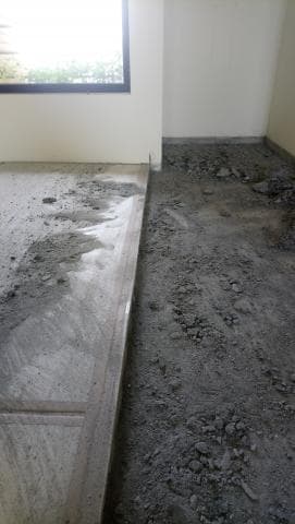 這張照片是正在翻新的房子，照片中可以看到地板正在施工，其中一部分已經鋪好了新的水泥地磚，而另一部分則還在施工中，可以看到許多灰塵和碎石。