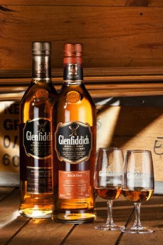 這張「兩瓶酒和兩個酒杯」的照片是兩瓶蘇格蘭威士忌，其中一瓶是格蘭菲迪 Rich Oak，另一瓶是格蘭菲迪 15 年，旁邊有兩個酒杯。