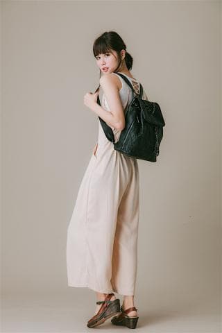 這張「女性時尚」的照片是一位穿著米色長褲，背著黑色揹包的年輕女性，她穿著一雙棕色涼鞋，笑容燦爛，顯得自信而優雅。