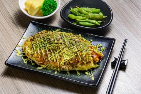 這張「煎蛋」的照片是一個放在黑色盤子上的煎蛋，上面覆蓋著綠色的醬汁，一旁還有一盤綠色的豆子。