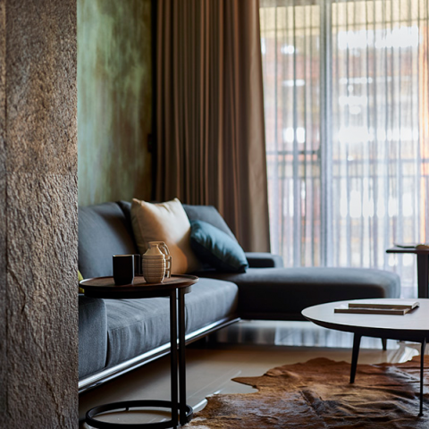 這張「現代客廳」的照片是一張灰色沙發，旁邊有一個小茶几，上面放著兩杯和一個花瓶。沙發旁邊還有一張咖啡桌。沙發後面的牆壁是綠色的，窗戶是白色的，窗簾是米色的。