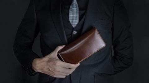 這張照片是一個穿著黑色西裝的男人，他拿著一個深棕色的皮革錢包。
