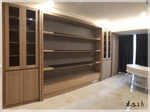 這張照片是一個現代化的客廳，最顯眼的是一面大型的木質置物櫃，有玻璃門、層架和抽屜，設計簡單但功能齊全，看起來很實用。