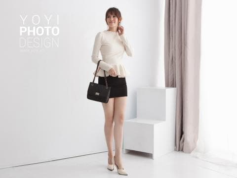 這張照片是一個穿著白色襯衫和黑色短裙的年輕女子，她正在拿著一個黑色的包包。