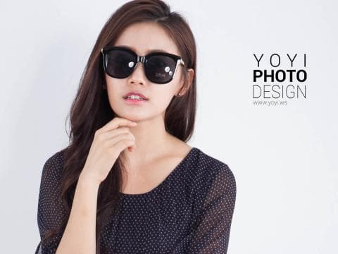 這張照片是一個戴著黑色太陽眼鏡的年輕女子，她身穿黑色點點上衣，手放在下巴附近。