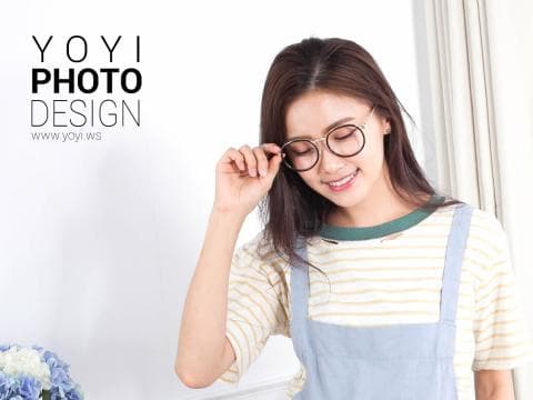 這張照片是一個年輕女子戴著眼鏡，穿著條紋上衣和牛仔背心，用手扶著眼鏡，露出溫柔的笑容。