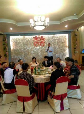 這張照片是一場婚宴的現場，主要部分是婚宴的餐桌，桌上擺滿了菜餚，賓客們圍坐在餐桌邊，喜氣洋洋。