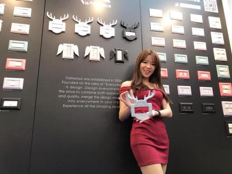 這張照片是一個展覽會，一個穿著紅色洋裝的女生拿著一個鹿頭造型的產品。