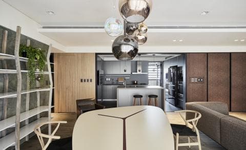 這張室內設計的照片是現代風格的客廳，可以看到一個大型餐桌、一個木製書架和一個灰色沙發。