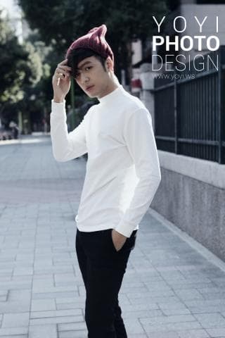 這張照片是一個戴著紅色毛帽的年輕男子，他穿著白色長袖上衣和黑色長褲，他站在一條水泥路上，看起來很時尚。