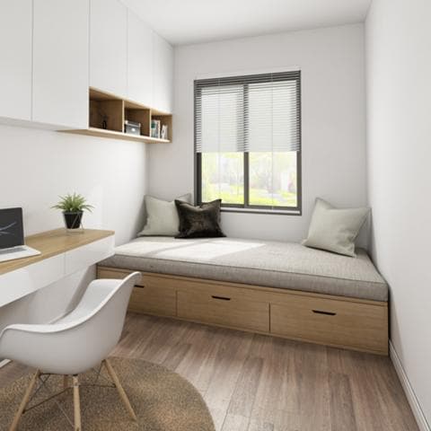 這張「小房間」的照片是一間簡約的臥室，配備一張床和一個書桌。床上有兩個枕頭，書桌上有椅子和一個綠色植物。牆上有一個白色櫥櫃，以及一個木質的層架，上面擺放一些物品。