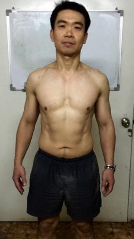 這張「肌肉男」的照片是一個身材健壯的男性，他穿著短褲，露出腹肌，背景是一面白板。