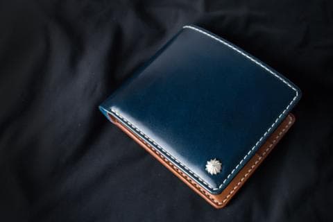 這張照片是一個深藍色的皮革錢包，中間有一顆銀色的星星圖案，周圍是淺棕色皮革縫邊。