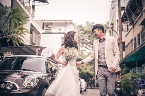 這張照片是一對新人在城市街頭的婚紗照，照片最重要的是新郎新娘的互動，新郎穿著白色西裝，新娘穿著白色婚紗，兩人手牽手，互相看著對方，洋溢著幸福的笑容。