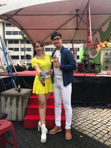 這張照片是一個男人和一個女人站在一個舞臺上。男人穿著藍色外套和白色褲子，女人穿著黃色連衣裙，他們都手持麥克風，看起來像是在主持活動。