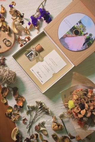 這張照片是一張婚禮的禮物盒，裡面裝著一個小小的玻璃瓶，瓶子裡裝著精緻的乾燥花，瓶口還綁著一個精美的緞帶。