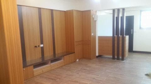 這張照片是一間客廳，最顯眼的是一面大型的木質電視櫃，它佔據了牆壁的大部分空間，設計簡潔，以實用為主，櫃體表面採用木紋紋路，散發著溫馨自然的氣息。