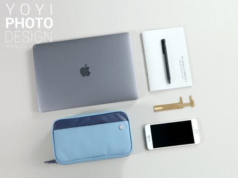 這張照片是一個現代化的工作空間，主要重點是擺放在白色桌面上的藍色筆記本電腦包。它旁邊還有一臺銀色的筆記型電腦，一個白色筆記本和一支黑色筆。整體畫面簡單俐落，展現出現代工作風格。