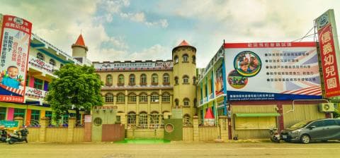 這張「幼稚園」的照片是一棟彩色的城堡建築，外面有許多招牌。建築物看起來很新，有很多窗戶，也有庭院和遊樂設施。