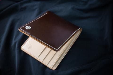 這張「皮革錢包」的照片是，一個深棕色皮革錢包，有縫線細節，和一個銀色的裝飾。
