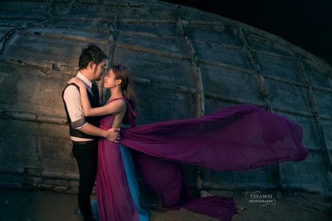 這張照片是一對情侶在古老的建築物前擁抱。男的穿著黑色西裝，女的穿著紫色長裙。他們的臉上都洋溢著幸福的笑容，非常甜蜜。