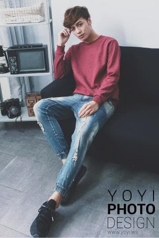 這張照片是一個年輕男子坐在沙發上，穿著紅色毛衣和牛仔褲，他看起來很時尚和放鬆。