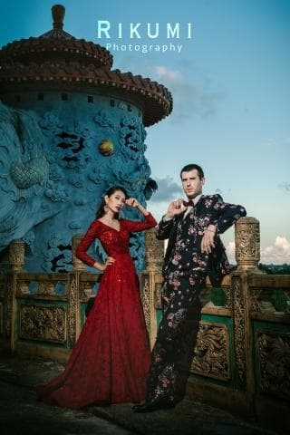 這張「婚紗照」的照片是一個穿著紅色的婚紗，站在一個古色古香建築前的女性和一個穿著黑色西裝的男性。