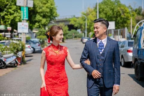 這張照片是一對新人，新郎穿著藍色格紋西裝，新娘穿著紅色婚紗，他們走在街上，看起來很幸福。