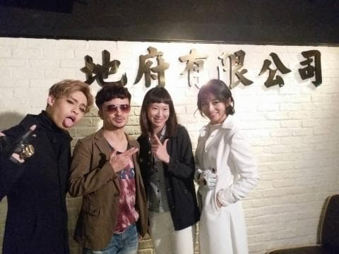 這張「四個年輕人站在牆壁前」的照片是，牆上有一塊寫著「地府有限公司」的金色招牌，照片中的人看起來很開心。