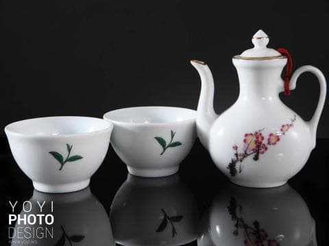 這張「茶具」的照片是兩個白色茶杯和一個白色茶壺，茶壺上繪有粉紅色花朵和綠色樹葉。茶杯上也繪有綠色樹葉。