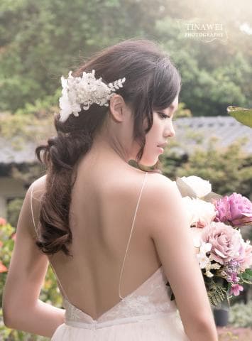 這張照片是一名穿著白色婚紗的新娘，她戴著精緻的花朵頭飾，露出美麗的鎖骨和背部曲線。
