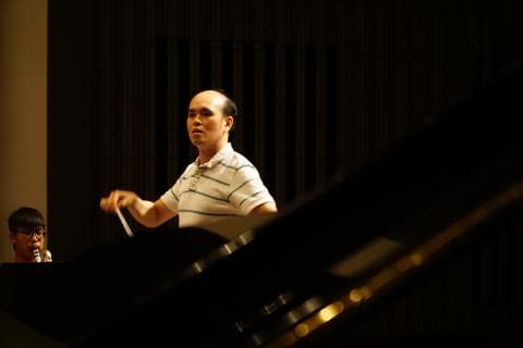 這張「指揮家」的照片是，一名男性指揮家正在臺上指揮樂團，他穿著白襯衫，手持指揮棒，面容嚴肅，專注地指揮著樂團。