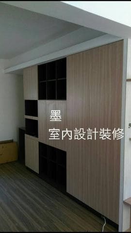 這張照片是一間房子的牆壁上的木櫃，櫃子分成兩個部分，左邊是一個開放式的架子，右邊是一個門板櫃。櫃子表面是木紋的，看起來很自然。櫃子上方有一塊白板，上面寫著「室內設計裝修」，顯然這是一個裝修完成的房子的牆壁。