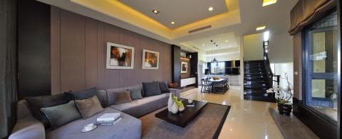 這張「現代住宅」的照片是一個寬敞明亮的客廳，有著舒適的灰色沙發和一張木質茶几。牆上掛著兩幅畫，房間的另一頭是通往餐廳和樓梯的走廊。