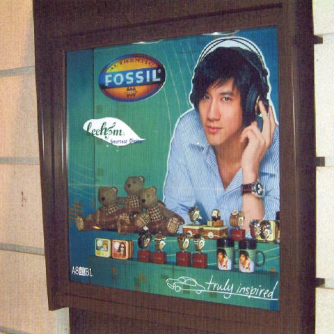 這張照片是一個廣告牌，上面是一位戴著耳機的年輕男性，身穿藍白條紋襯衫，手持一隻Fossil 手錶，並配有品牌標誌和口號。