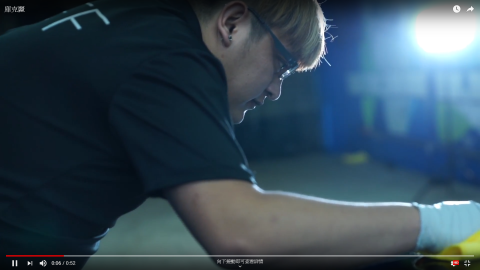 這張「一個男人在擦拭一輛車」的照片是，他戴著眼鏡，穿著黑色T恤，正在用黃色的布擦拭一輛車的表面。