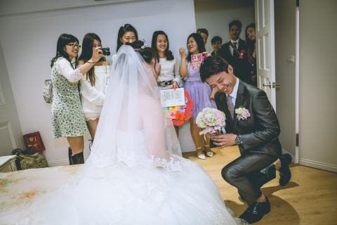 這張照片是一對新人結婚的照片，新娘穿著婚紗，新郎單膝跪地，手拿花束，向新娘求婚。