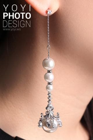 這張照片是一個戴著珍珠耳環的女性。耳環是銀色的，上面有許多珍珠和水晶。耳環的末端有一個精緻的設計，看起來像一個小皇冠。