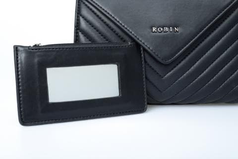 這張照片是一個黑色的小包，包上有一個小鏡子。鏡子嵌在一個小皮套裡，皮套上有一個拉鏈。包包上印著 ROBIN 的字樣。
