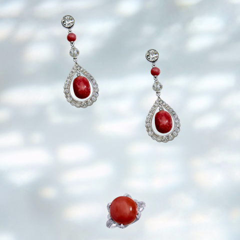 這張照片是三件珊瑚和鑽石首飾，其中最重要的是一對耳環。耳環的設計精緻，以銀色金屬製成，並鑲嵌著閃亮的鑽石。耳環的中心是鮮紅色的珊瑚珠，與鑽石形成鮮明的對比。