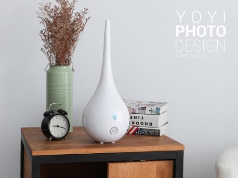 這張「加濕器」的照片是一個白色的加濕器，放在一個木質的桌子上，旁邊還有一個鬧鐘和一瓶花。