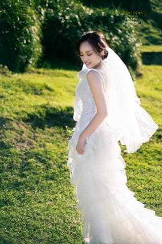 這張照片是一個穿著婚紗的新娘，她站在綠草地上，背對著鏡頭，臉上帶著幸福的笑容，裙襬飄逸，美不勝收。